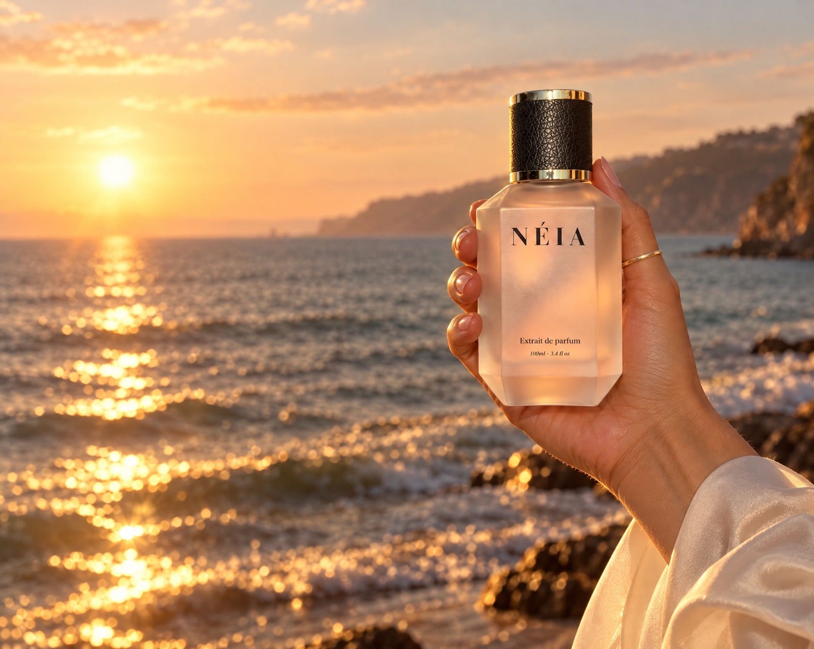 A hand holding Silk Musk 100ml up to a sunset over the sea