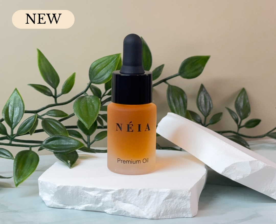 Néia premium perfume oil bottle on a white stone surface with green leaves in the background