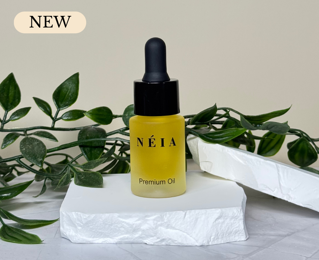 Yellow NEIA premium oil dropper bottle on a white surface with green leaves in the background