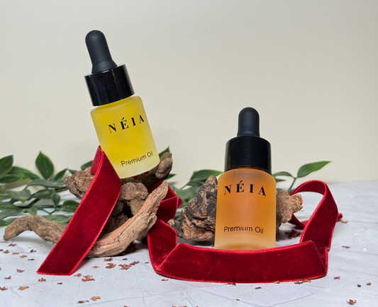 Two bottles of NÉIA Premium Oil on a white surface with a red ribbon and natural elements.