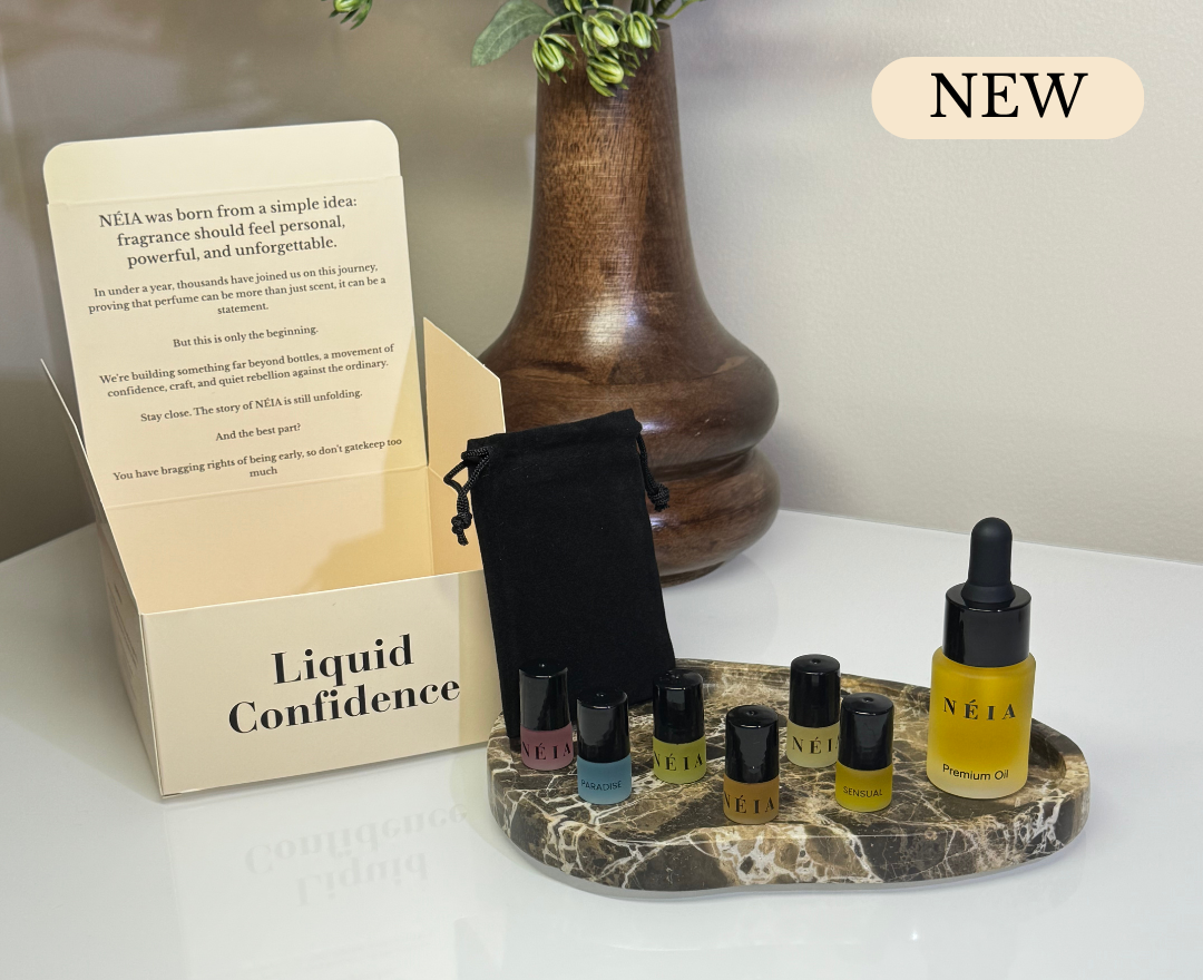 Set of small perfume oil bottles on a marble stand with 'NÉIA' branding, next to a box labeled 'Liquid Confidence'.
