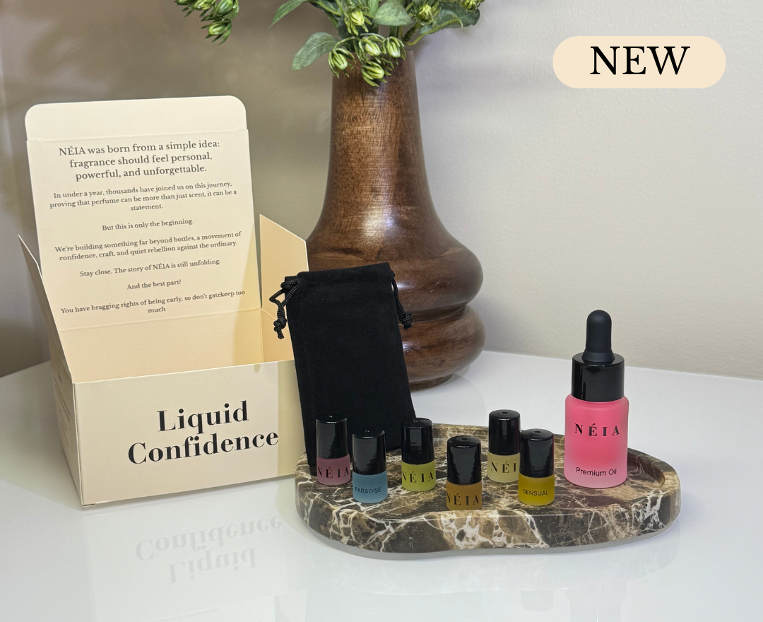 Set of perfume oil bottles with a dropper and packaging on a marble stand, with 'NEW' label above.