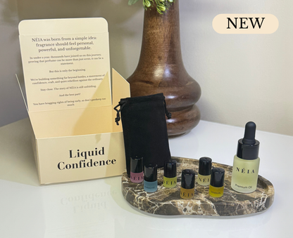 Set of NEIA perfume bottles on a marble stand with packaging and a wooden vase in the background.