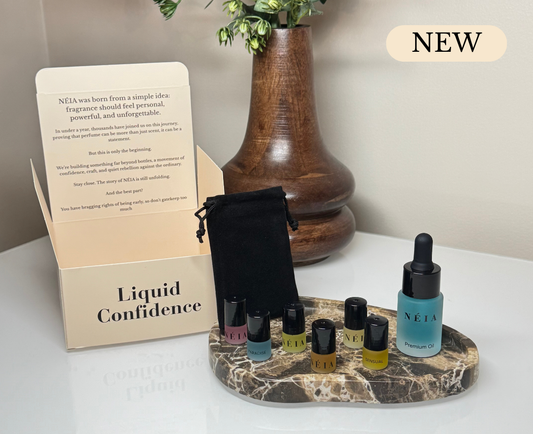 Set of perfume bottles on a marble stand with a box labeled 'Liquid Confidence' and a wooden vase in the background.