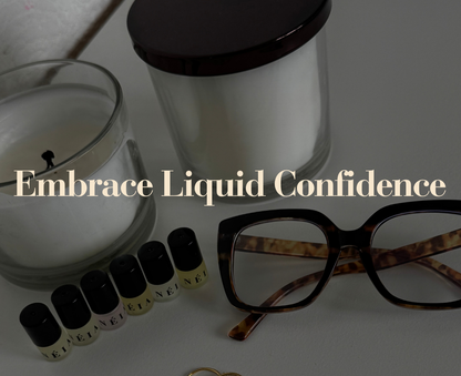 Candle, glasses, and small bottles with text 'Embrace Liquid Confidence' on a reflective surface.