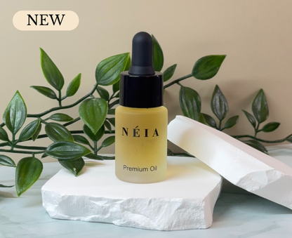 Néia premium perfume oil bottle with dropper on a white stone surface with green leaves in the background