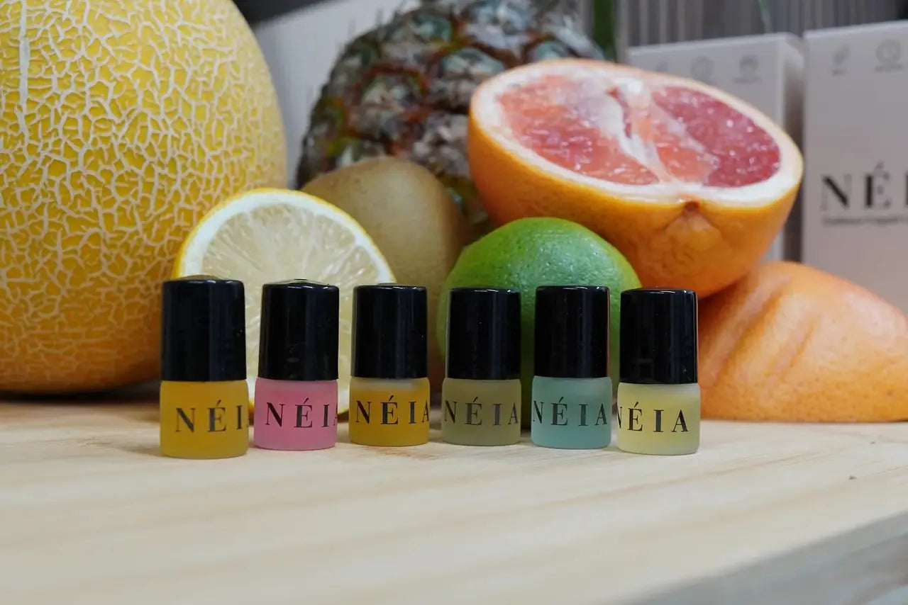 The six NÉIA women's perfume oils in a row on a wooden counter, with grapefruit, lemon, lime and melon behind them.
